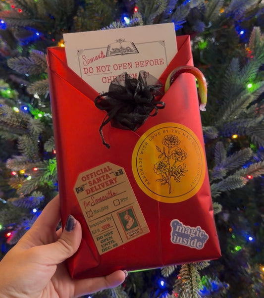 Red gift bag with festive text and a black bow, held in front of a decorated Christmas tree.