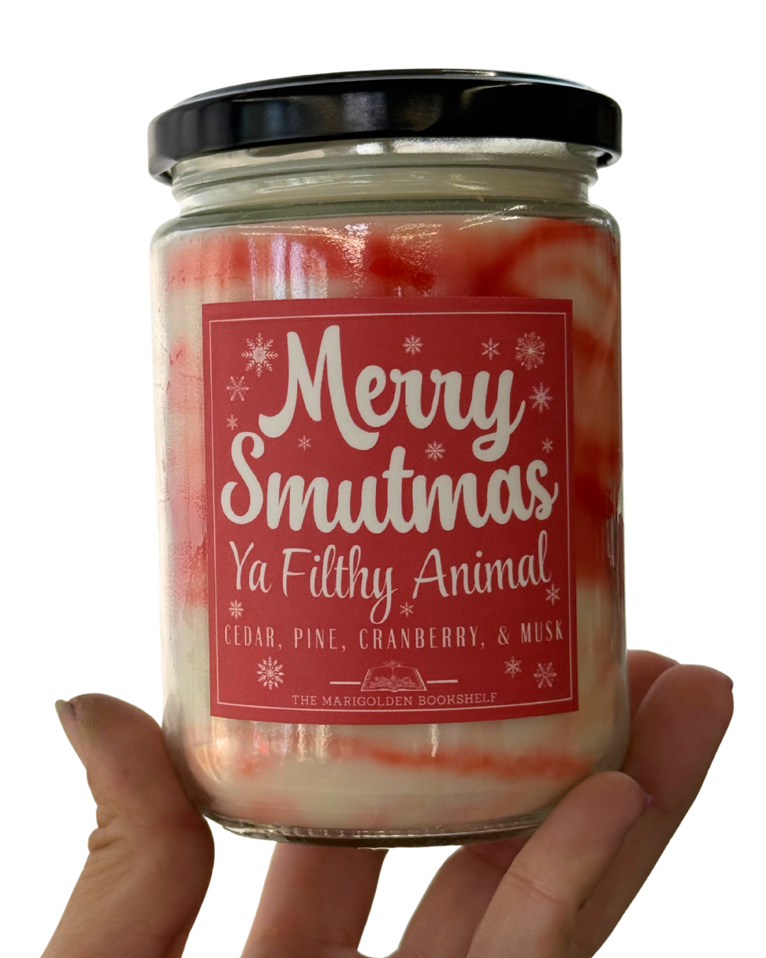 A glass candle jar with a black lid with a sticker that says 'Merry Smutmas Ya Filthy Animal' and 'Cedar, Pine, Cranberry, & Musk'