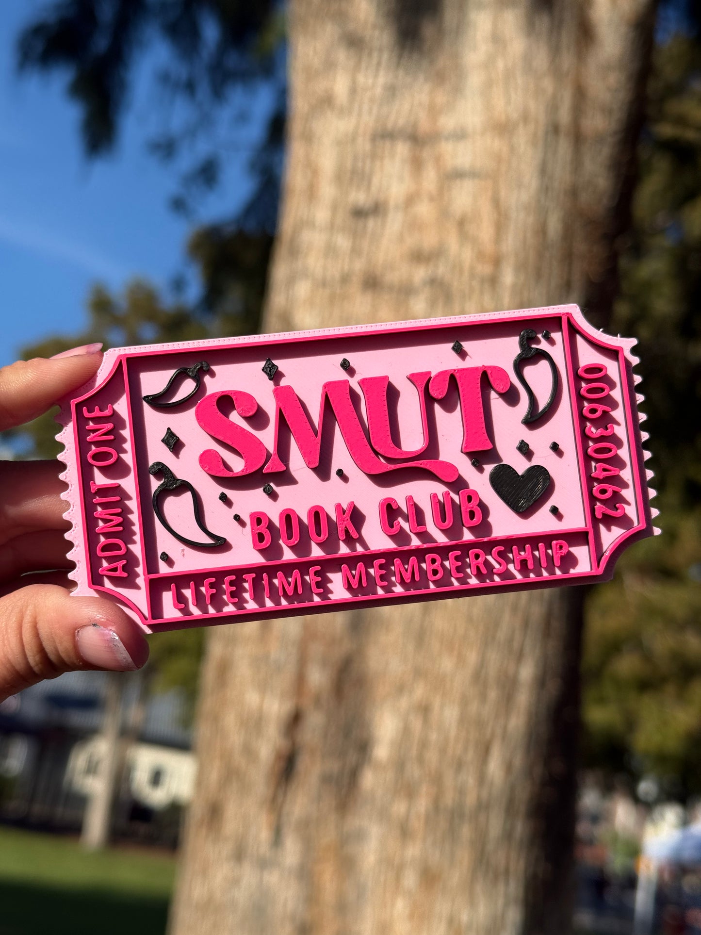 A pink 3D printed theater ticket to 'Smut Book Club' with 'Admit One', 'Lifetime Membership', and the numbers '00630462' written on the edges