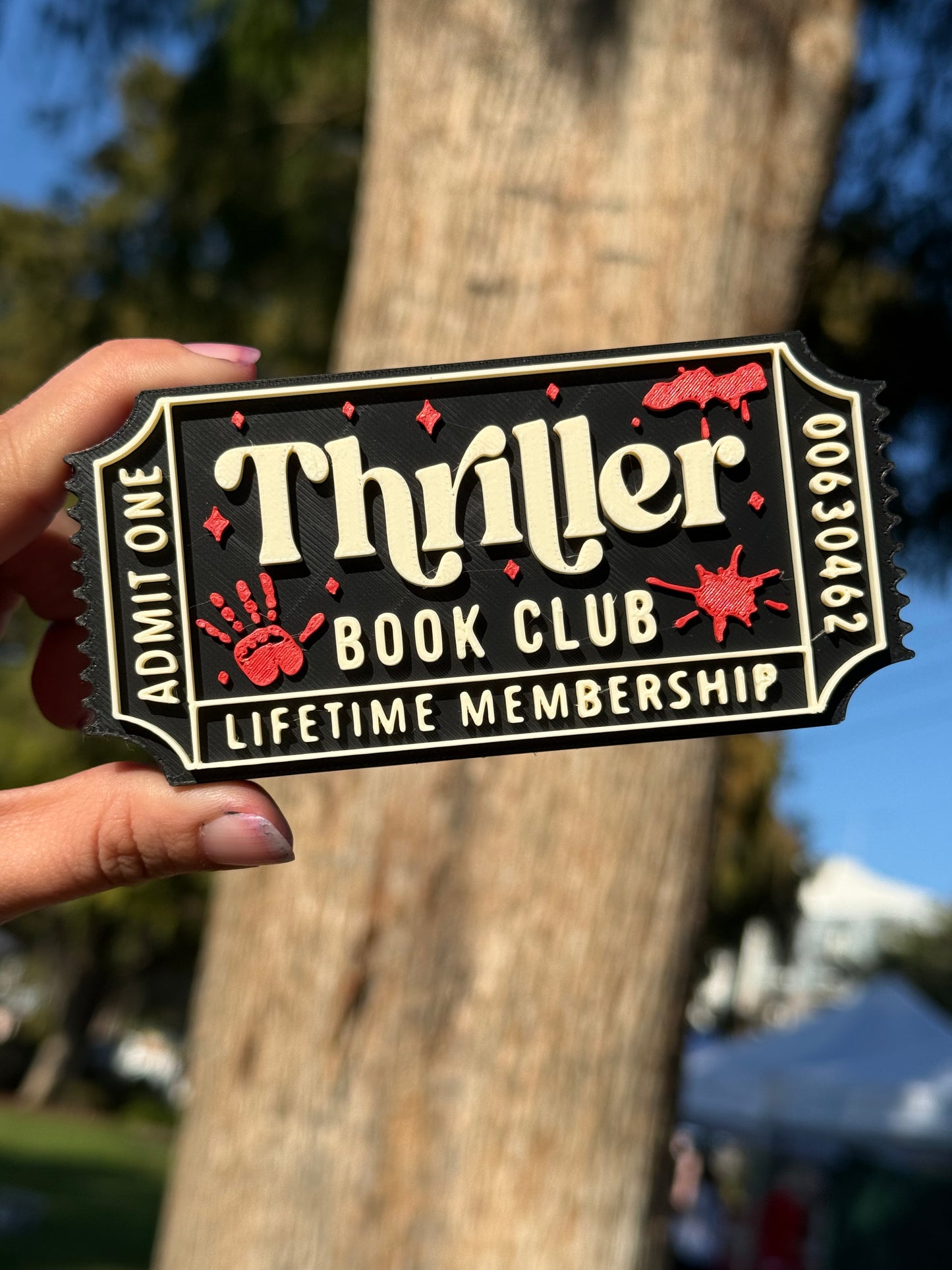 A black 3D printed theater ticket to 'Thriller Book Club' with 'Admit One', 'Lifetime Membership', and the numbers '00630462' written on the edges