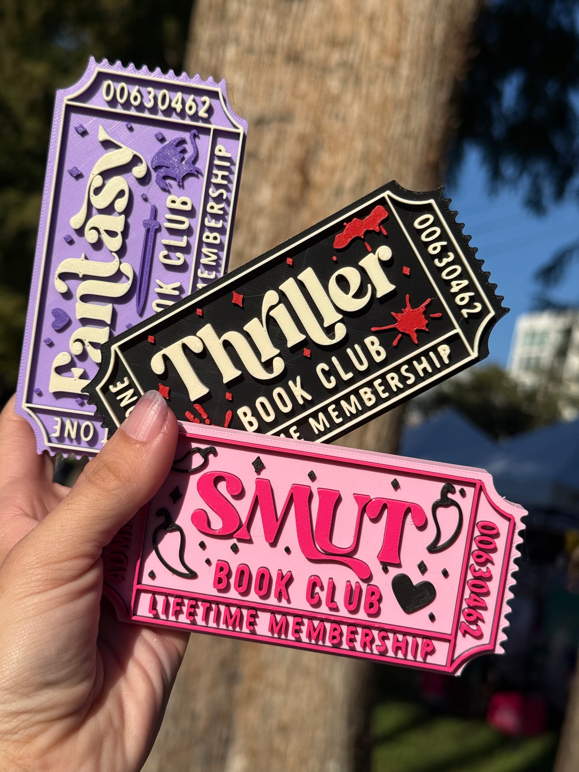 Three 3D printed theater tickets to 'Fantasy Book Club', 'Thriller Book Club', and 'Smut Book Club' with 'Admit One', 'Lifetime Membership', and the numbers '00630462' written on the edges